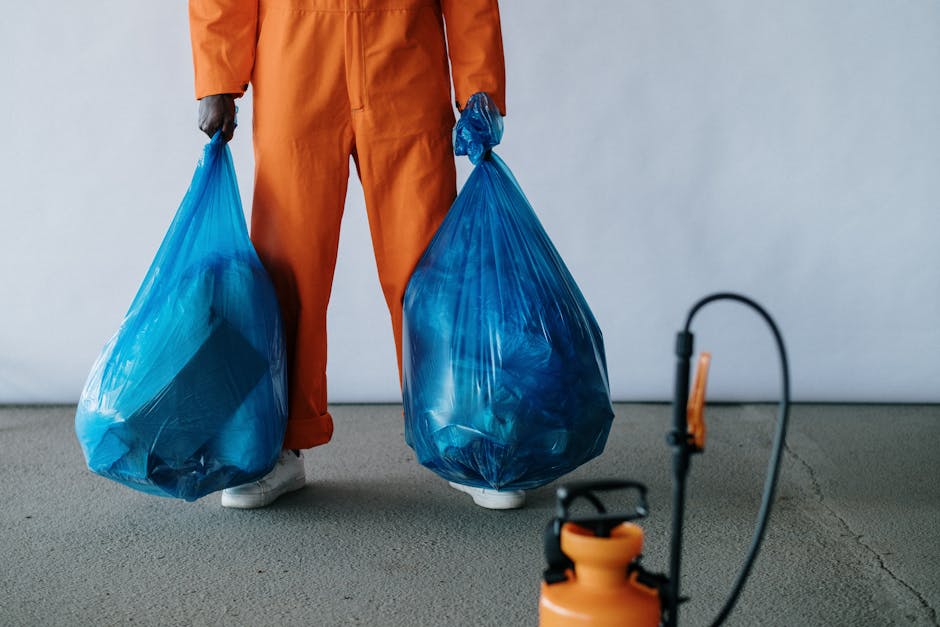 A white moving van parked on the street with its rear door open, revealing a partial view of the interior. Outside the van, three large blue garbage bags filled with packaging materials or discarded i